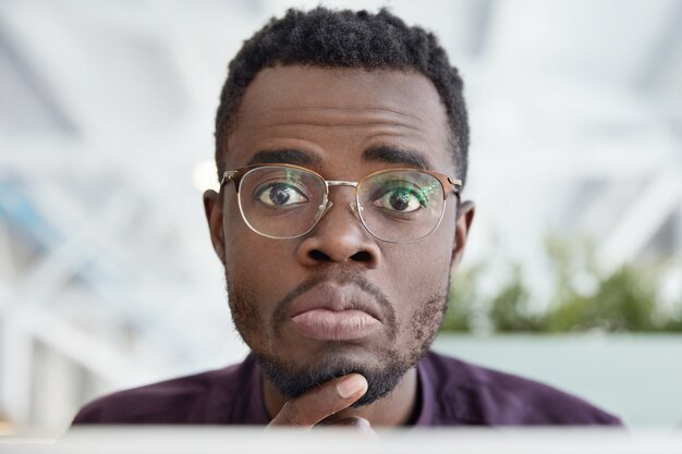 Close up shot of handsome African Americam male with dark pure skin, wears round spectacles and formal clothes