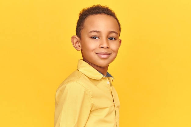 Close up shot of handsome friendly looking boy in yellow shirt smiling, being in good mood posing isolated against blank background with copy space