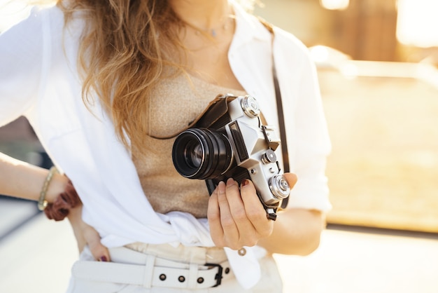 Immagine ravvicinata di una viaggiatrice felice e vestita alla moda con la macchina fotografica in un clima soleggiato