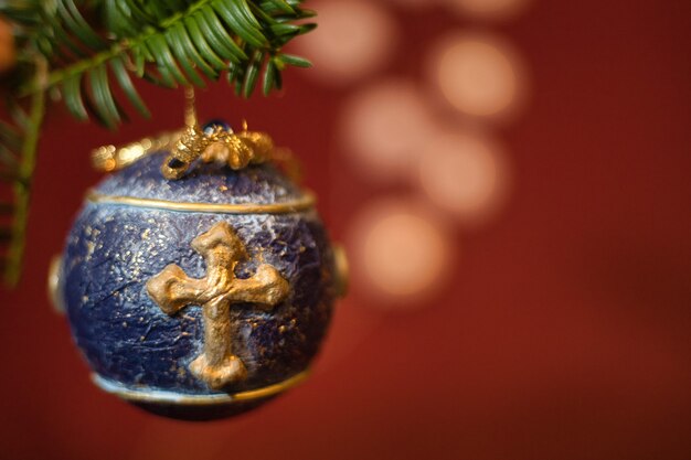 Close-up shot of isolated blue Christmas tree ball decoration, with golden cross hanging on a green