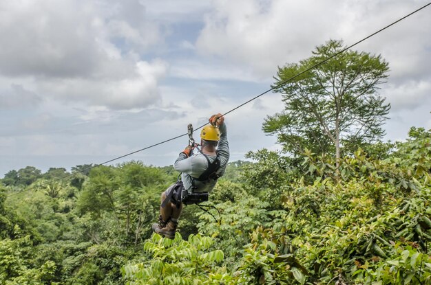 Close up shot of a man hanging and sliding on the zipline in a beautiful park cloudy sky