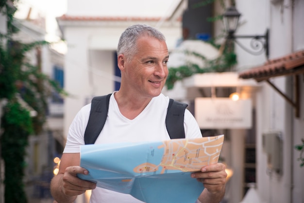 Close up shot of a mature man with a map while standing outdoors in the city on a summer day.