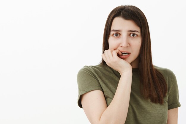 Close-up shot of nervous unsure and insecure female coworker messing up documents worried someone notice biting fingernails anxiously frowning standing intense over gray wall