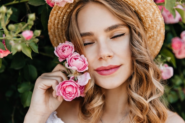 Бесплатное фото Крупным планом вдохновил кавказской женщины, держащей розовый цветок. открытый портрет изысканной блондинки охлаждая в саду.