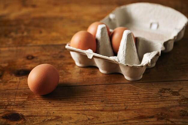 Free photo close up shot of an open recyclable egg carton with 3 eggs inside and one egg next to it on a brown grainy wooden table