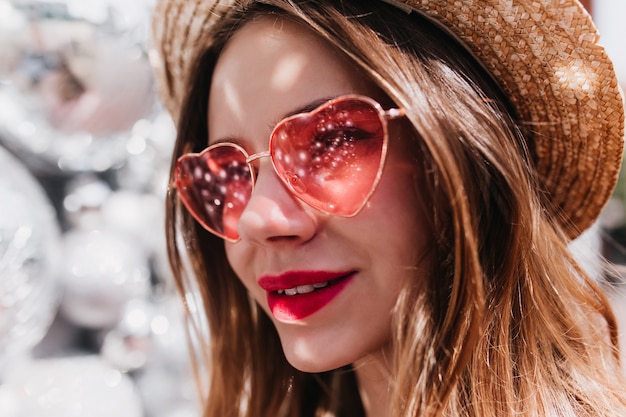 Foto gratuita colpo del primo piano della donna attraente pensierosa in cappello di paglia. debonair ragazza caucasica in eleganti occhiali da sole rosa che guarda lontano.