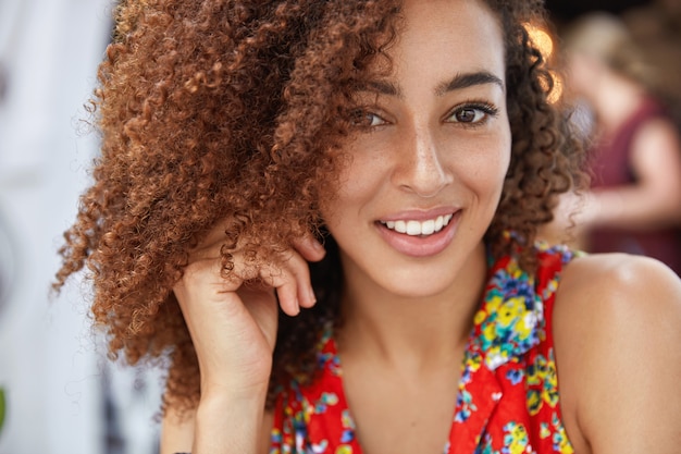 Close up shot of pleasant looking cheerful African American female with joyful expression, dressed in bright summer clothing