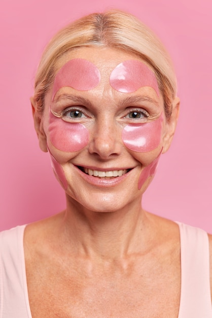 Close up shot of pretty mature aged woman applies moisturizing patches on face to reduce fine lines