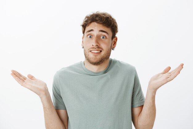 Close-up shot of questioned awkward handsome male in earrings, shrugging and spreading palms cluelessly, being unaware and knowing nothing what to do