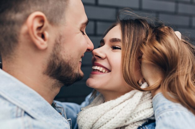 Close-up shot of smiling bearded man touching girlfriend's hair. Outdoor portrait of romantic laughing woman enjoying date.