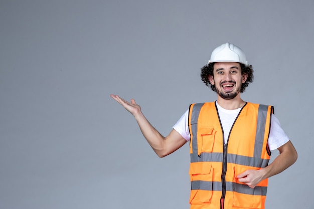 Immagine ravvicinata di un architetto maschio sorridente in giubbotto di avvertimento con casco di sicurezza e che punta qualcosa sopra la parete grigia dell'onda