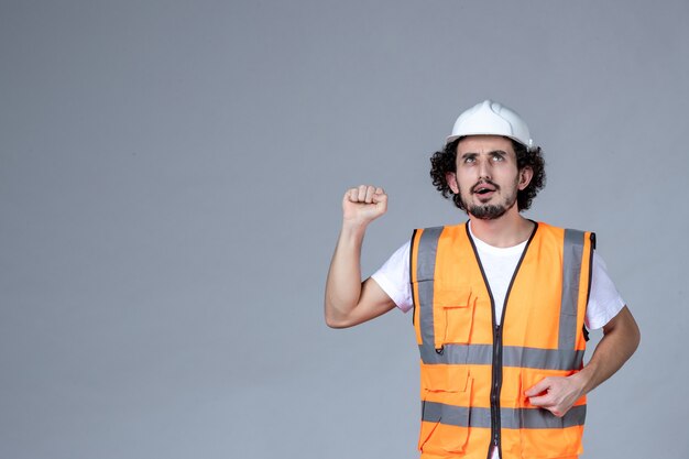 Close up shot of thinking male architect in warning vest with safety helmet and raising hand over gray wave wall