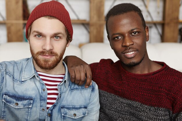 Close up shot of two attractive stylish male friends of different races relaxing at cafe