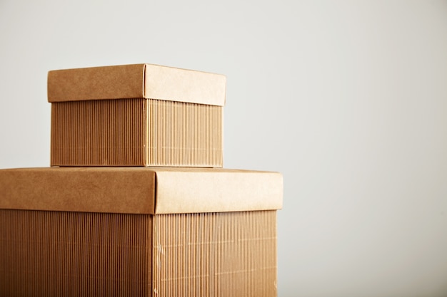 Close up shot of two similar corrugated cardboard square boxes of different sizes on top of each other isolated on white