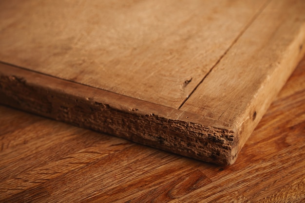 Free photo close up shot of a very old and battered chopping board with deep cuts, pieces missing lying on a rustic wooden table