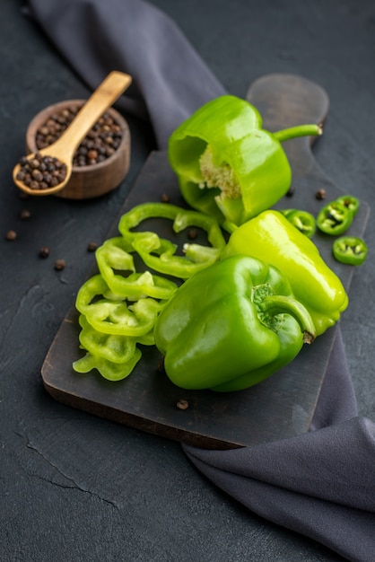 Foto gratuita immagine ravvicinata di peperoni verdi tagliati interi tagliati su tagliere di legno su superficie di colore scuro