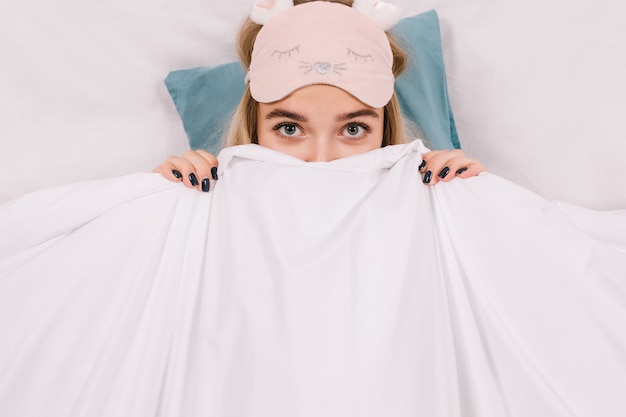 Free photo close-up shot of woman in sleep mask hiding under blanket