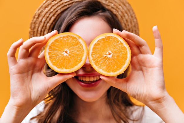 Close-up shot of young girl in boater covering her eyes with juicy oranges.