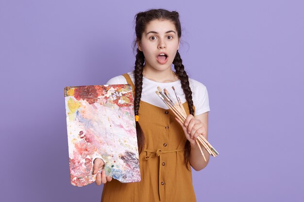 Close up shot of young woman artist holding color palette and paint brush in hands