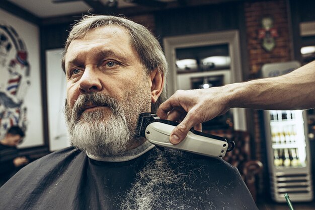 Close-up side view portrait of handsome senior bearded caucasian man getting beard grooming in modern barbershop.