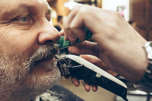 Close-up side view portrait of handsome senior bearded caucasian man getting beard grooming in modern barbershop.