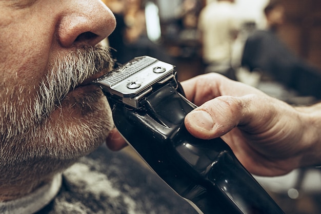 Close-up side view portrait of handsome senior bearded caucasian man getting beard grooming in modern barbershop.