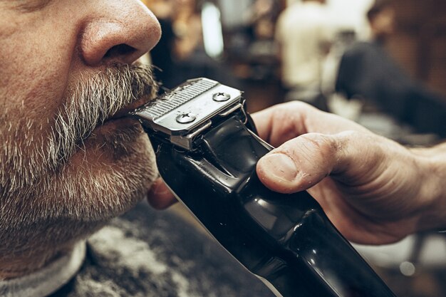 Портрет взгляда со стороны конца-вверх красивого старшего бородатого кавказского человека получая холить бороды в современной парикмахерскае.