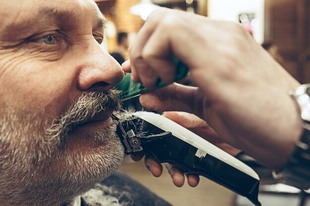 Бесплатное фото Портрет взгляда со стороны конца-вверх красивого старшего бородатого кавказского человека получая холить бороды в современной парикмахерскае.