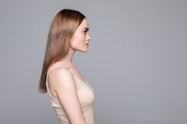 Close up side view of young woman standing isolated grey wall