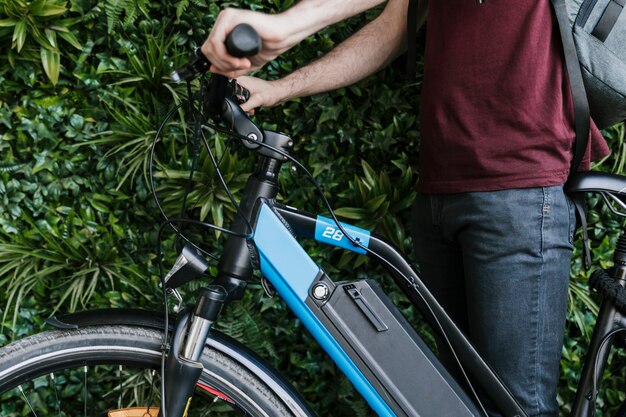 Close up sideways cyclist holding e-bike with green wall background