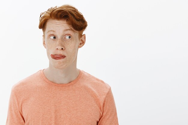 Close-up of silly and cute redhead man looking right curious and showing tongue