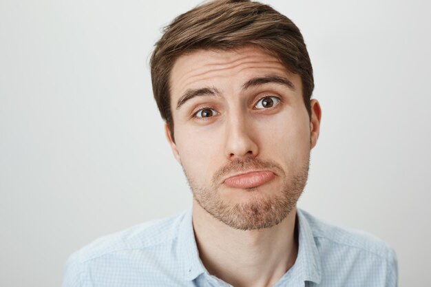 Close-up of silly and cute young man pouting, begging for favor