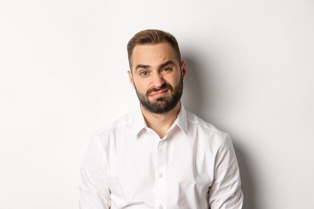 Close-up of skeptical bearded man grimacing displeased, dont like something, standing reluctant against white background.