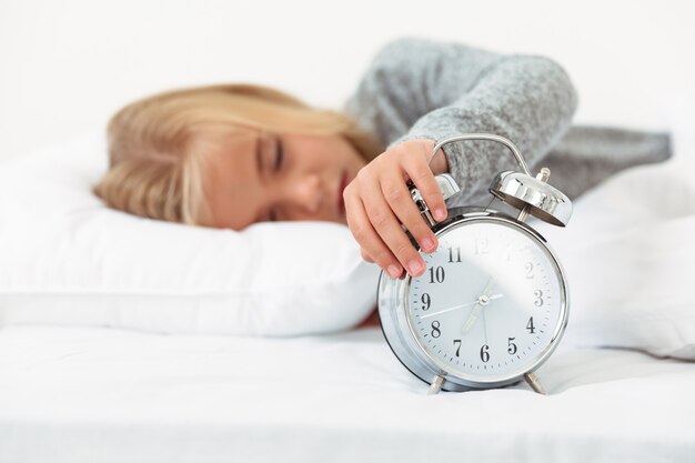 Close-up of sleepy little girl turned off alarm clock in her bedroom