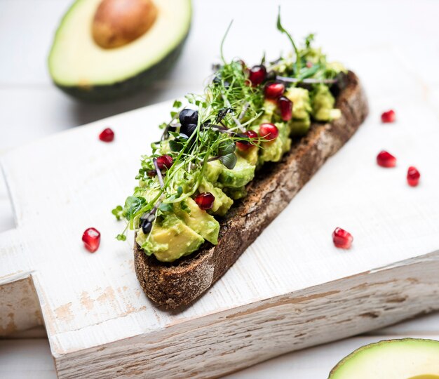 Close-up slice of bread with avocado pasta and pomegranate