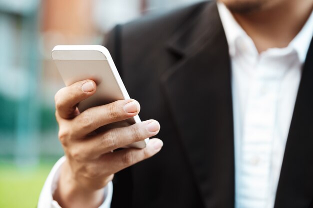 Foto gratuita close-up elegante uomo d'affari che indossa abito nero moderno e camicia bianca e texting sul telefono cellulare intelligente