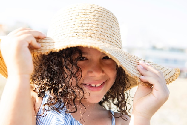 해변에서 모자를 쓰고 웃는 소녀를 닫습니다
