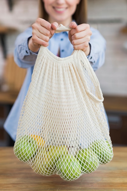 Free photo close-up smiley woman holding reusable bag with fruits