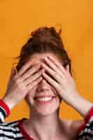 Free photo close-up smiley woman with orange background covering her eyes