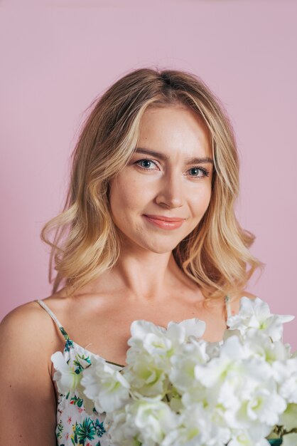 Close-up of smiling blonde young woman holding white flower in hand