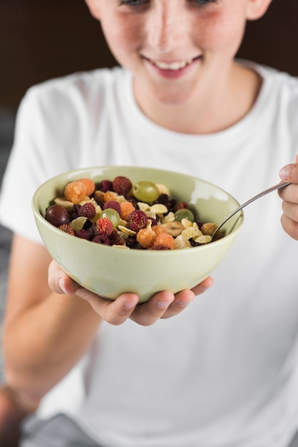 Close-up of a smiling boy holding bowl of fruit salad