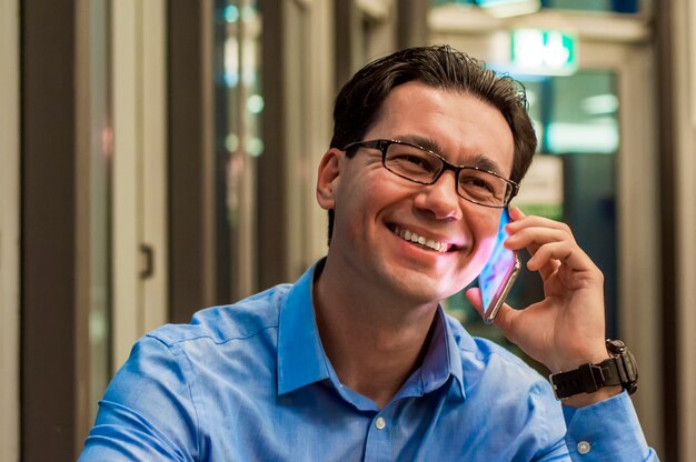 Закройте улыбается бизнесмен, используя современный смартфон, Молодой счастливый человек, работающих в его офисе и проведение сотовый телефон