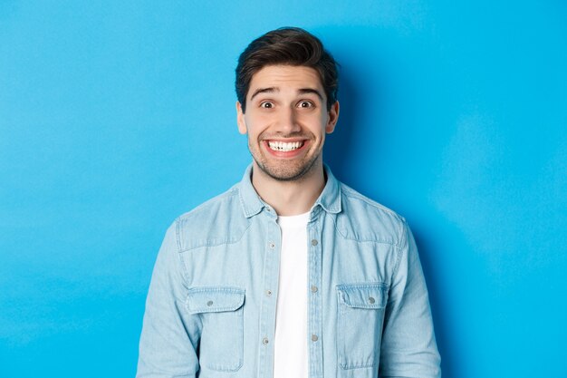 Close-up of smiling excited man with beard, looking amused at advertisement, standing against blue background