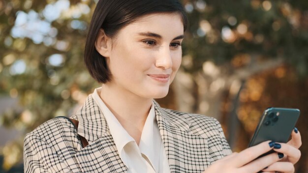 Close up smiling female entrepreneur looking happy texting on smartphone about new deal working on city street Stylish girl outdoor