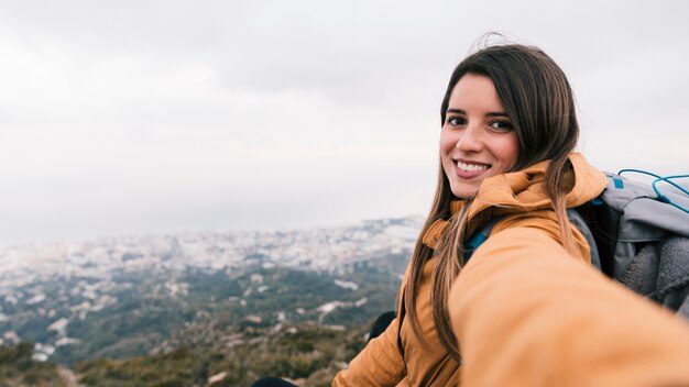 山の上に携帯電話でselfieを取って笑顔の女性ハイカーのクローズアップ