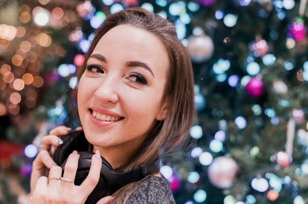 よそ見クリスマスツリーの近くのヘッドフォンを着て笑顔の女性のクローズアップ