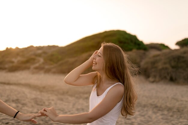 Close-up of smiling girl holding her friend's hand at beach