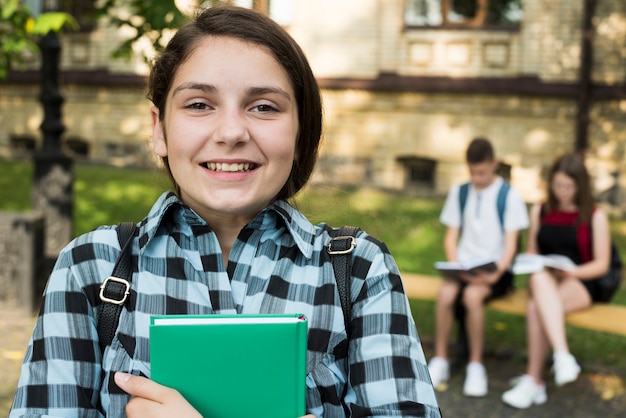 Foto gratuita chiuda su del libro sorridente della tenuta della ragazza della high school in mani