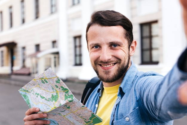 Крупным планом улыбающийся человек, держащий карту принимая селфи на открытом воздухе