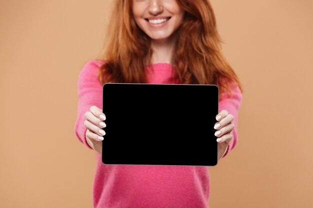 Закройте улыбающегося довольно рыжая девушка показывает цифровой планшет с пустой черный экран